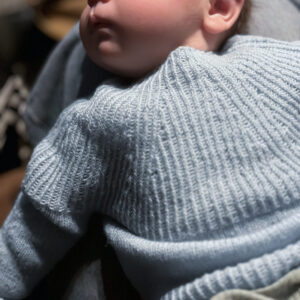 Baby lying on back waaring blue handknit sweater