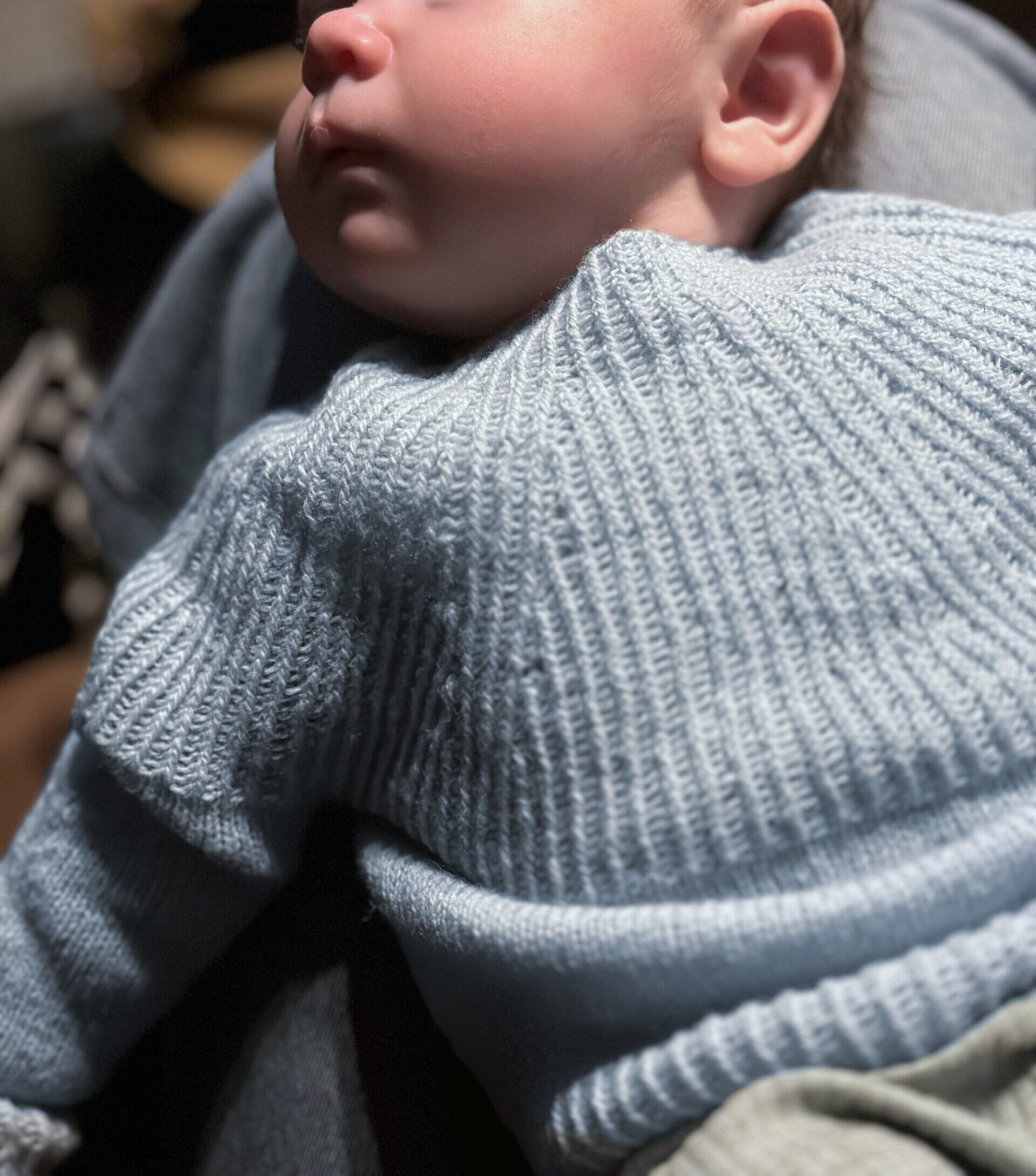 Baby lying on back waaring blue handknit sweater
