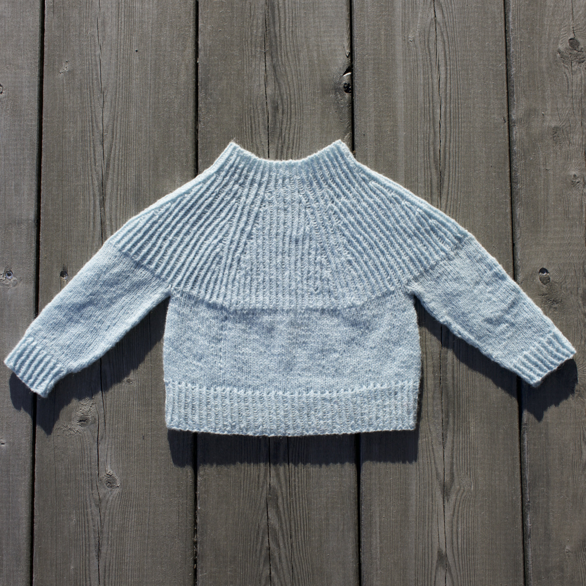 handknitted blue baby sweater on wood floor